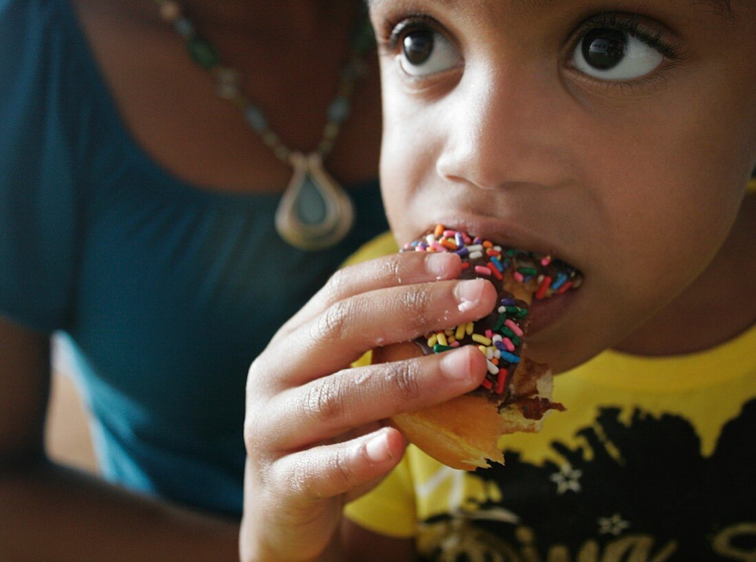 Kleines Mädchen isst einen Doughnut mit bunten Zuckerstreuseln