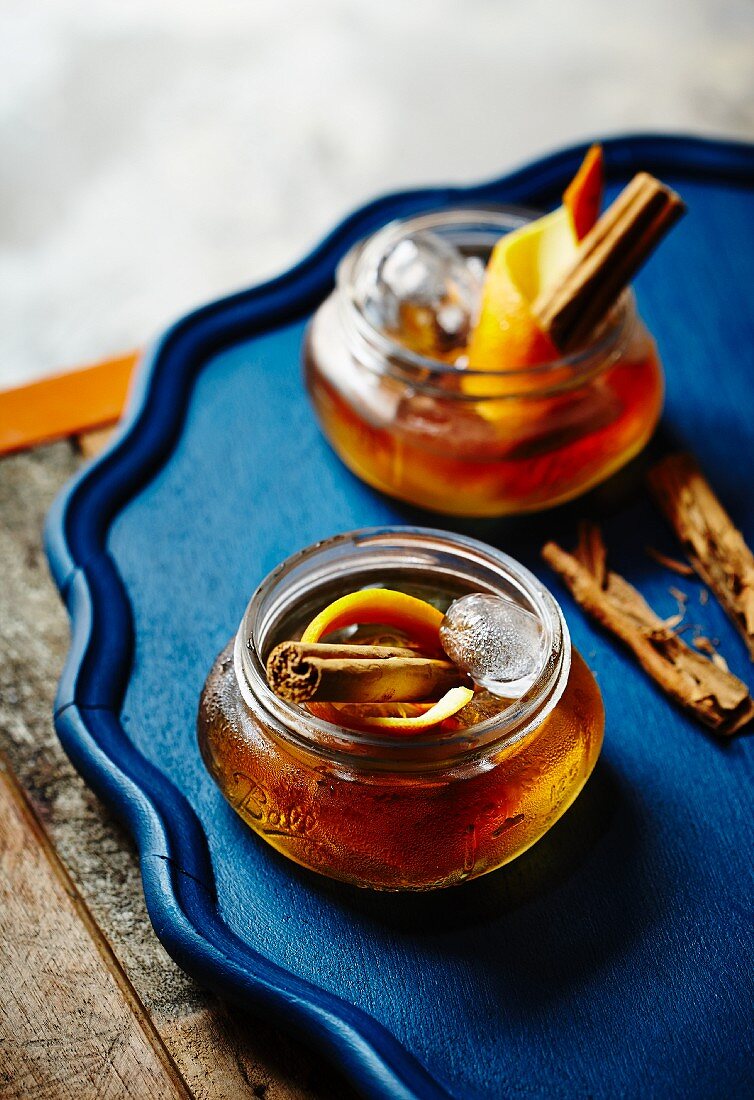 Two 'Old Fashioned' cocktails with cinnamon sticks and orange peel