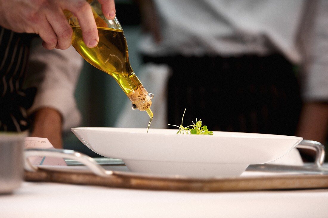 Chef adding olive oil to dish during service at working restaurant