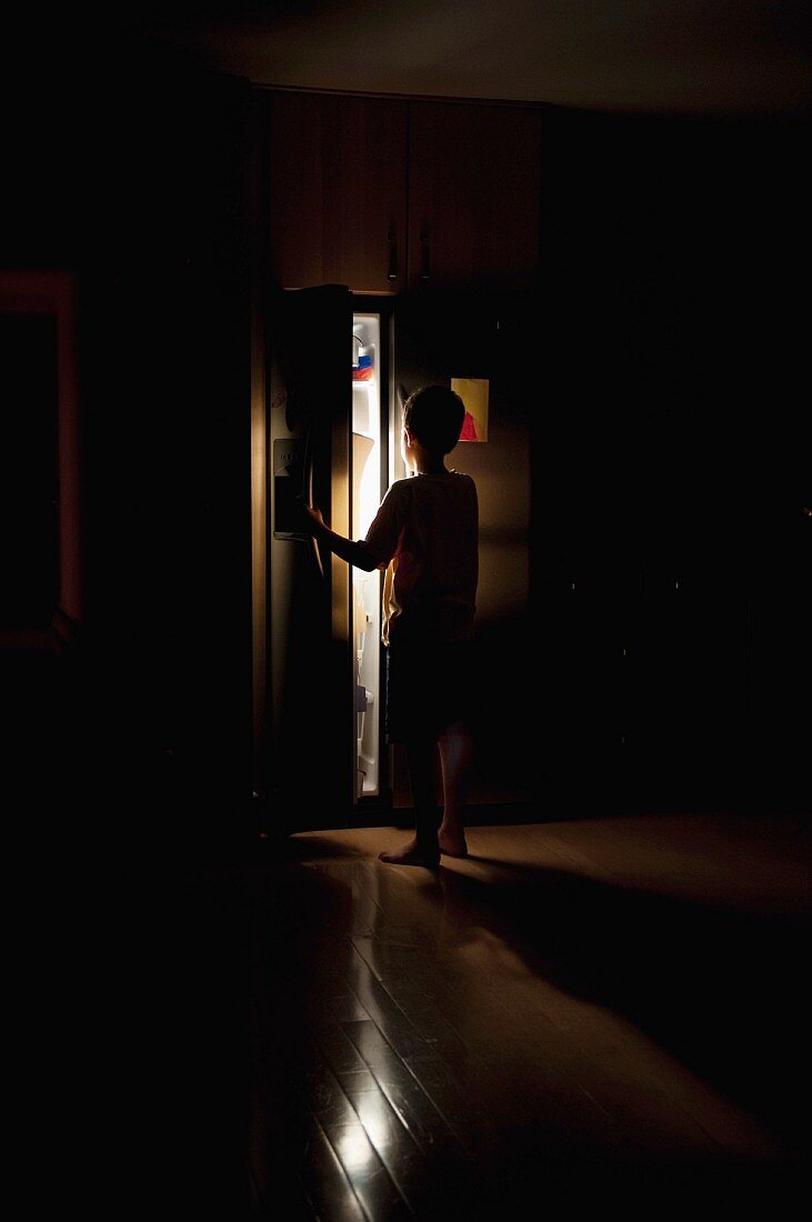 Junge in der dunklen Küche in den Kühlschrank schauend