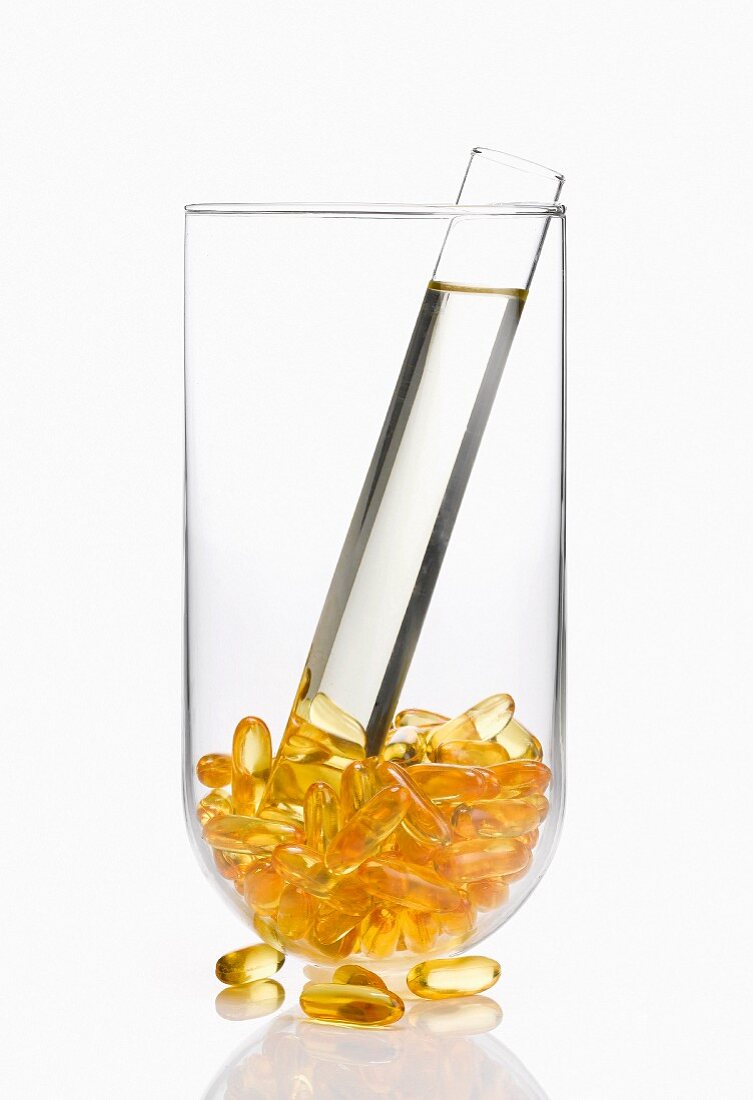 Vitaminkapseln und Röhrchen mit Flüssigkeit in einem Glas