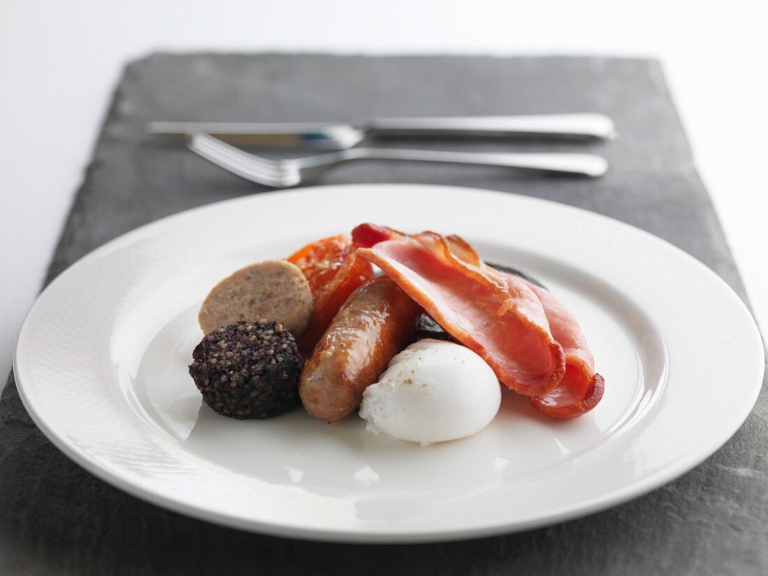 Englisches Frühstück mit Wurst, Speck, gebratenen Tomaten, Blutwurst, Leberwurst und pochiertem Ei