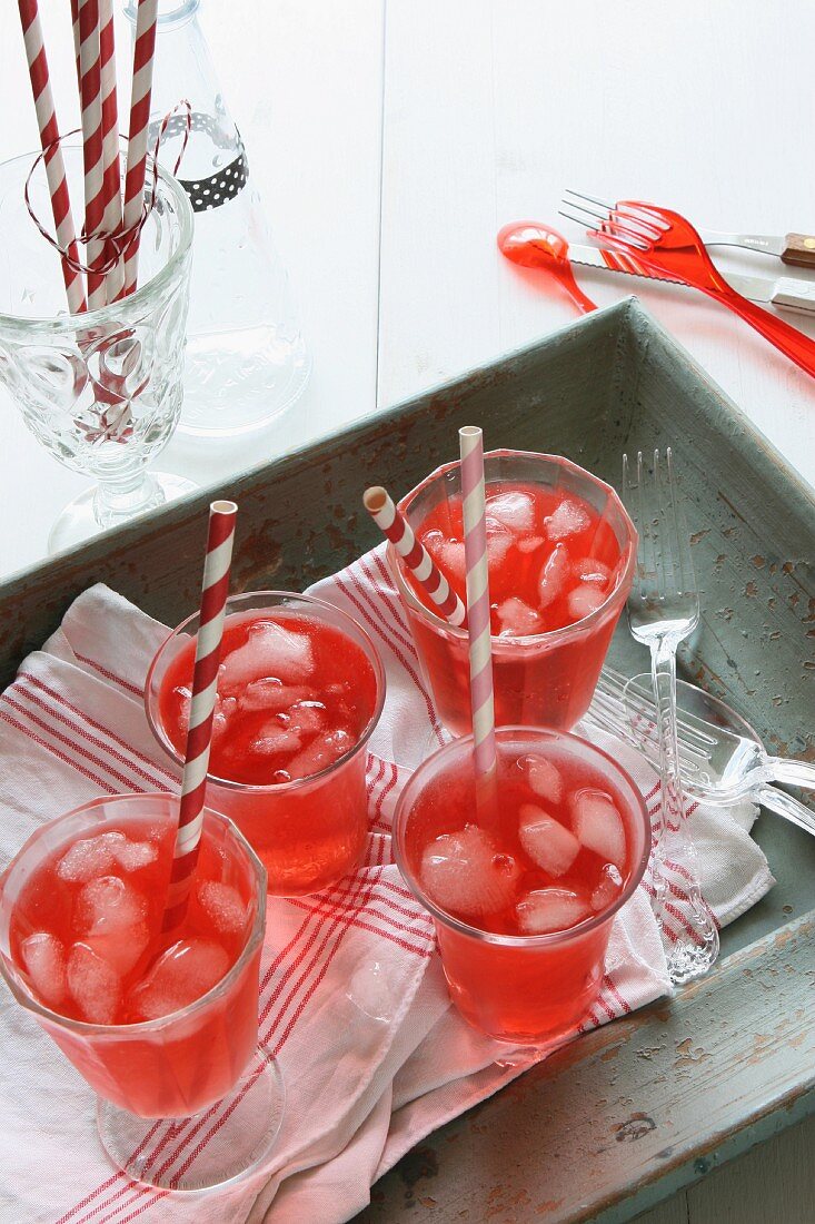 Rote Limonade mit Eiswürfeln und Strohhalm auf Holztablett
