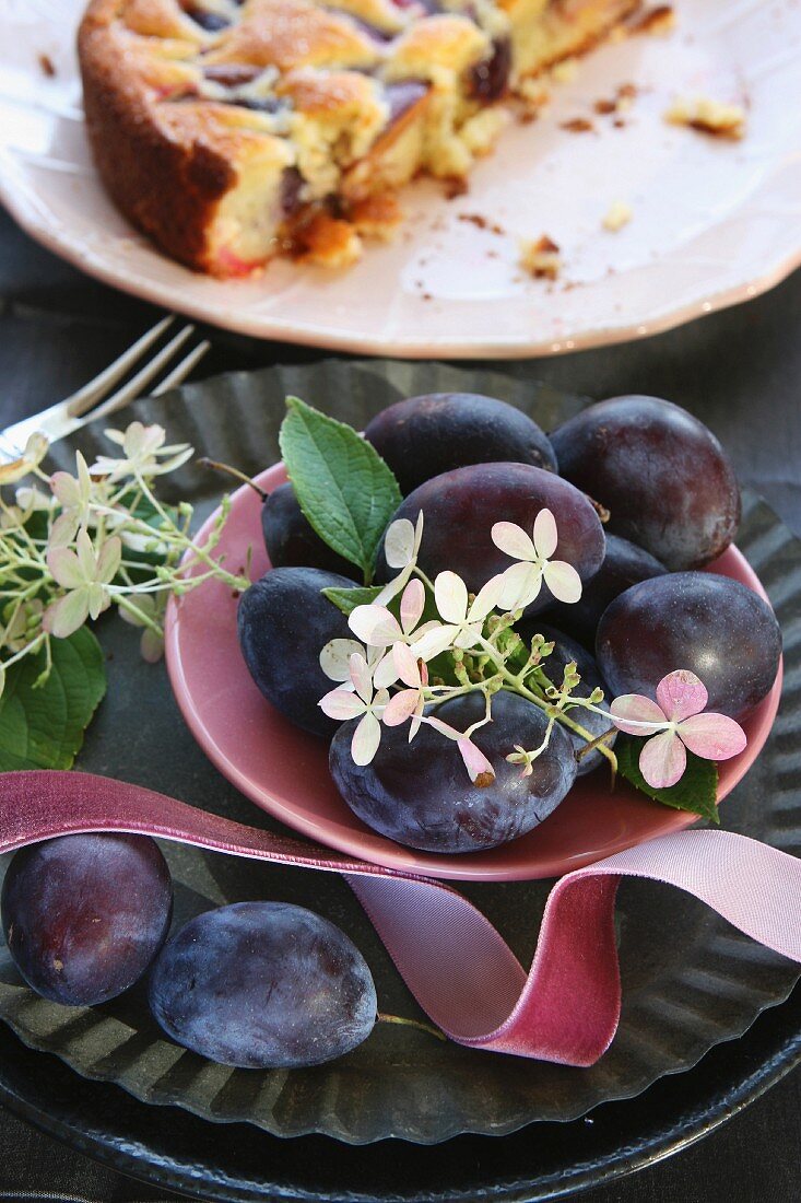 A bowl of plums in front of a sliced plum cakes