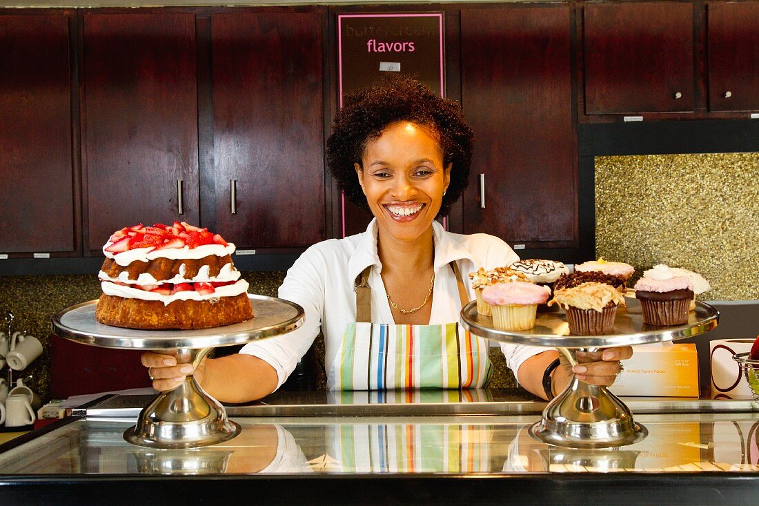 Frau stellt Kuchen und Cupcakes auf die Theke einer Konditorei