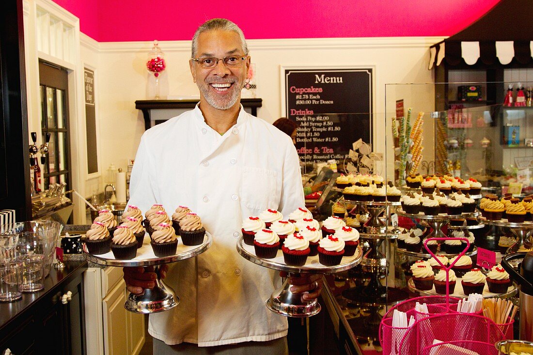 Mann zeigt Kuchenständer mit Cupcakes in der Bäckerei