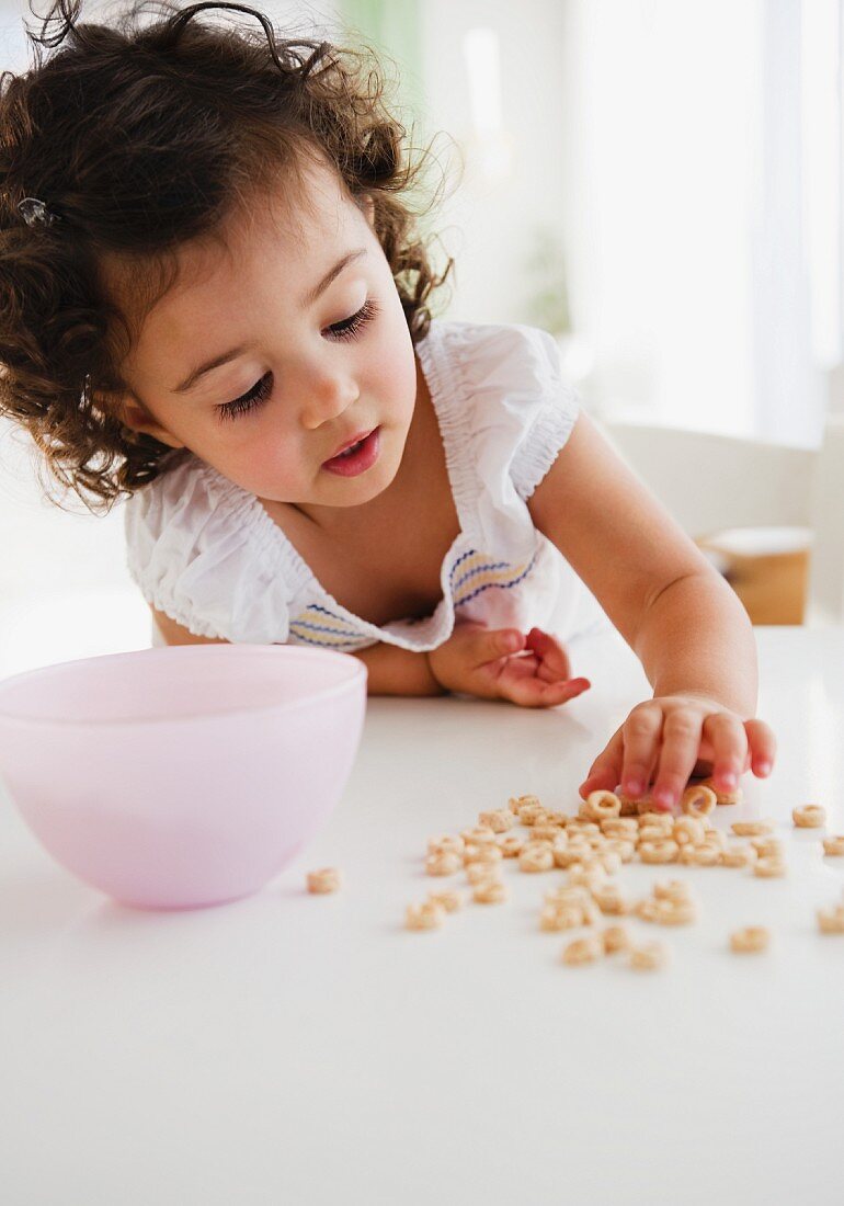 Kleines Mädchen greift nach verschütteten Cerealien am Tisch