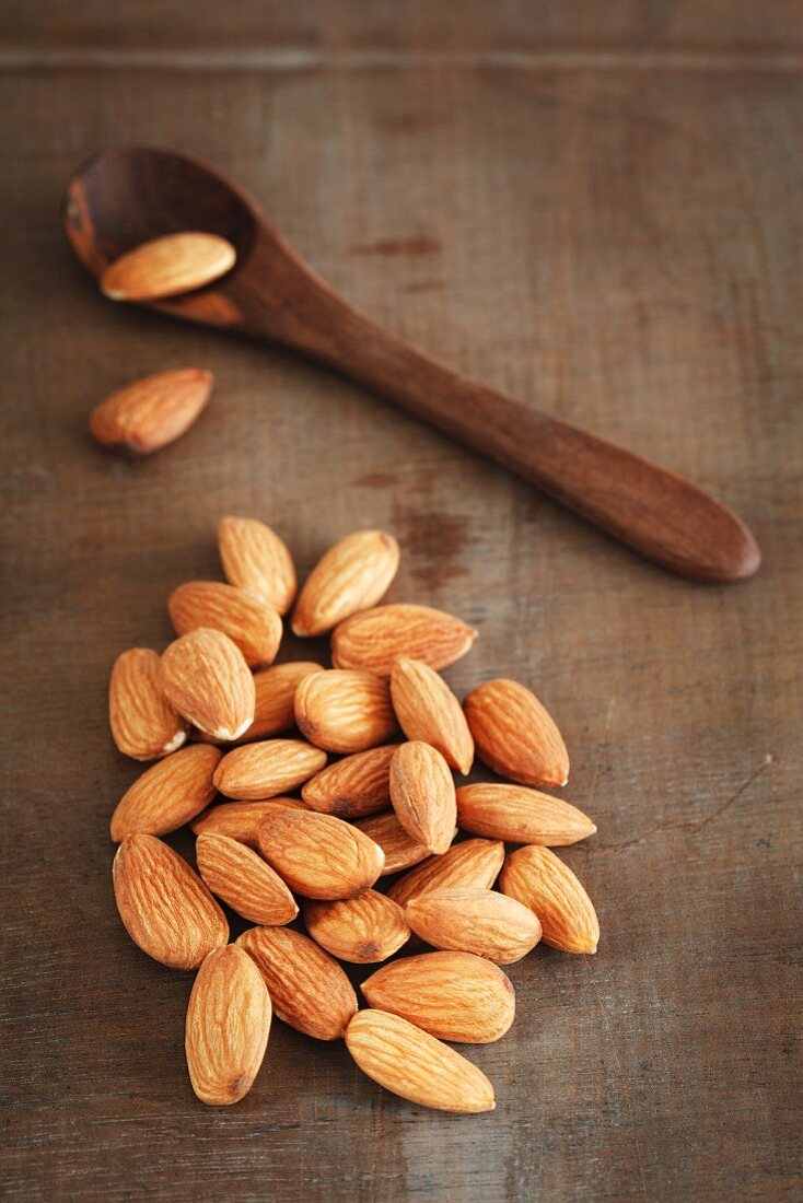 Almonds on a wooden surface with a wooden spoon
