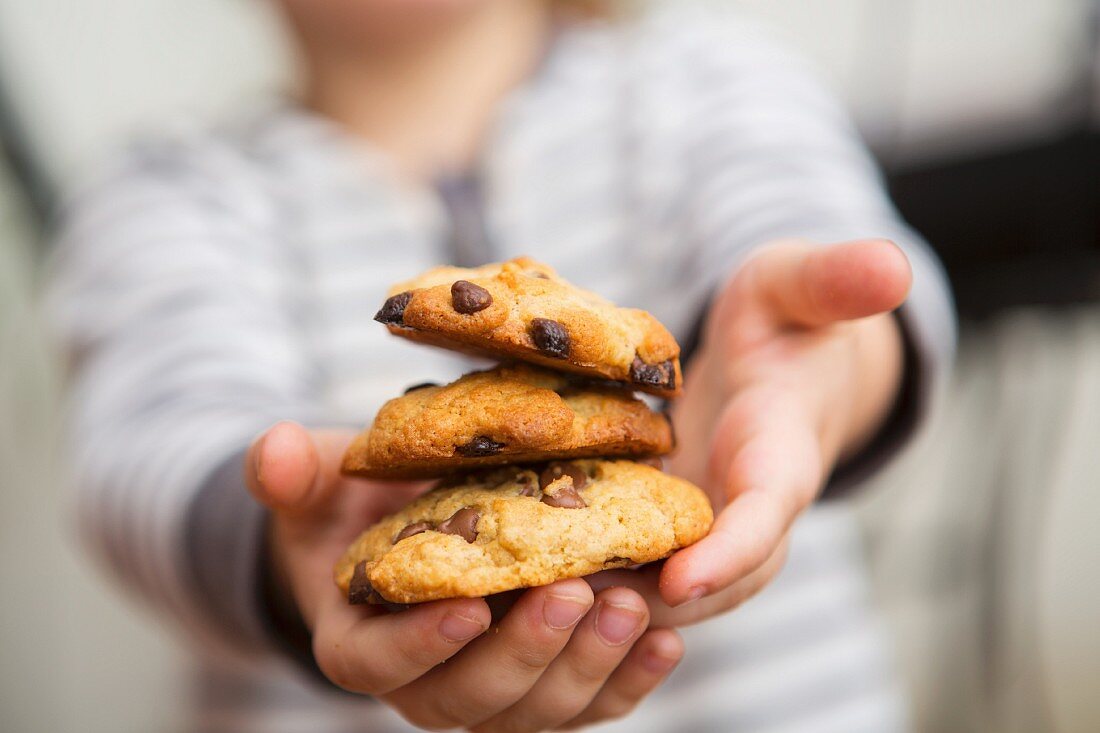 A child holding a stack of chocolate chip cookies