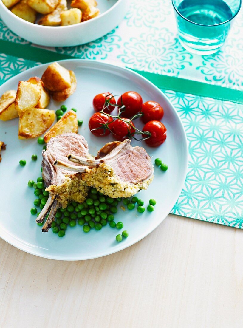 Lammrücken im Kräutermantel, serviert mit Erbsen, Kartoffeln und Tomaten