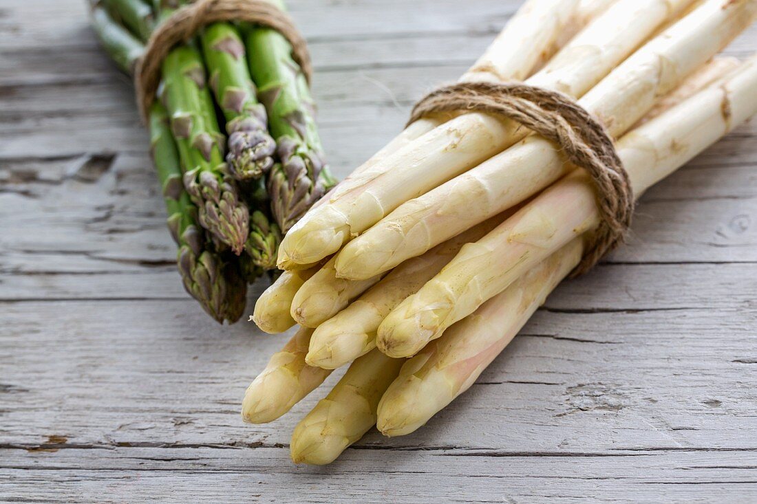 Green and white asparagus, tied in bundles, on a wooden surface