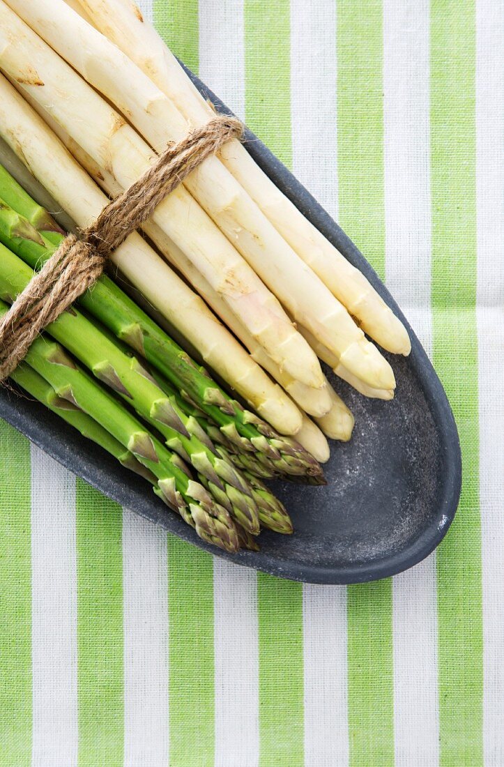 Green and white asparagus, tied in bundles, on a plate