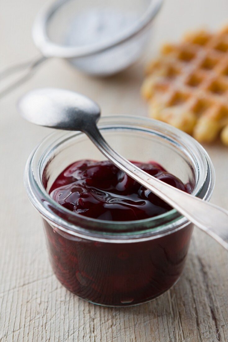 Cherry jam in a glass, waffles and icing sugar