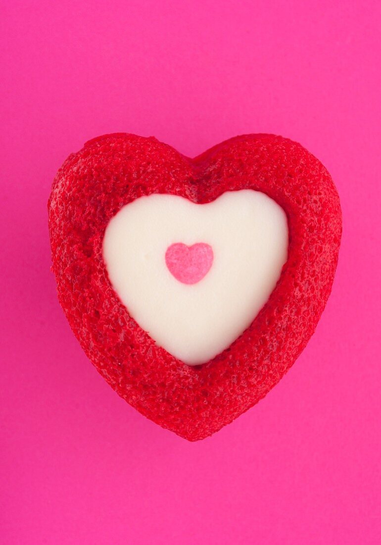Heart-shaped muffin with white chocolate topping on pink background
