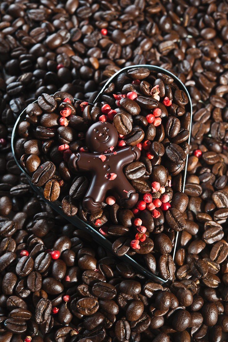 Schokoladenmännchen auf Kaffeebohnen und rosa Pfeffer in herzförmiger Ausstechform