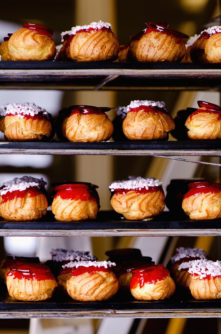 Choux buns with red caramel topping and sugar crystals on shelves in a bakery