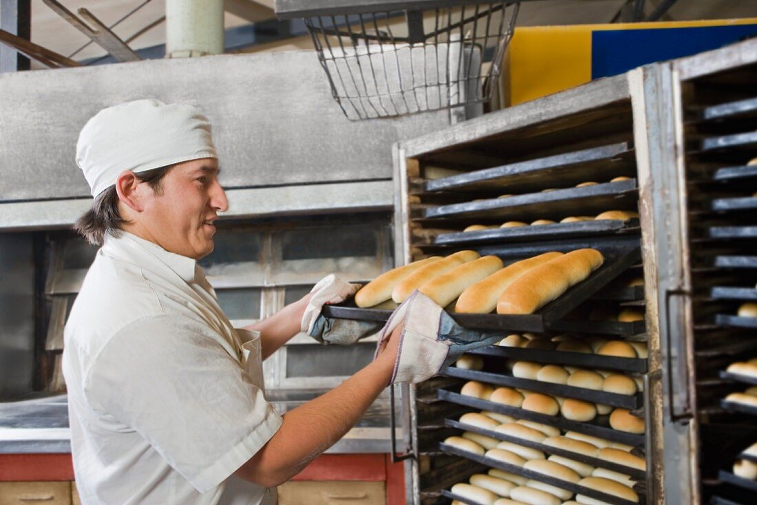 A baker with freshly baked rolls on a baking tray