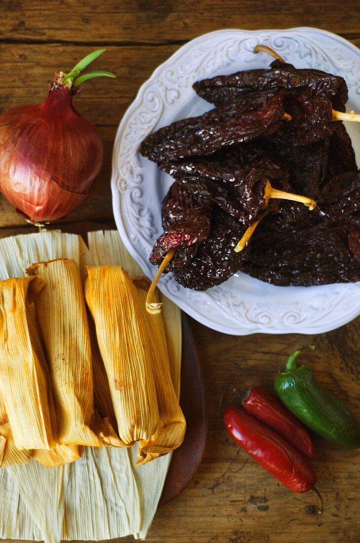 An arrangement featuring tamales, an onion and fresh and preserved chillis