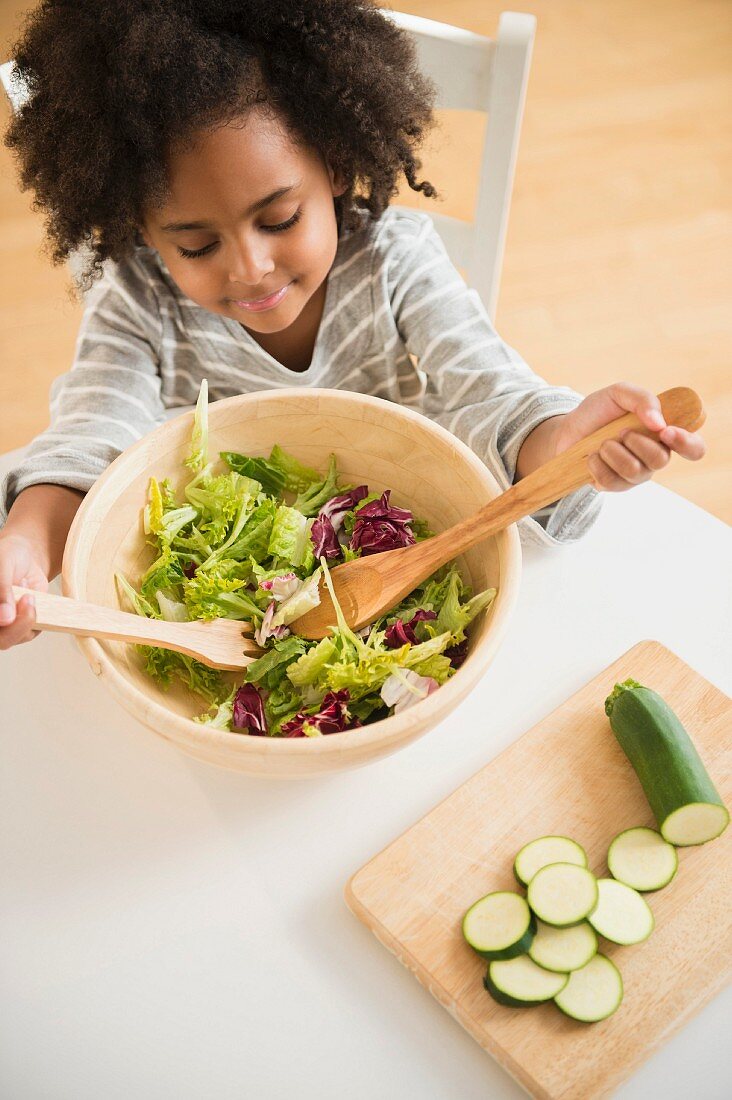 An African-American girl sitting at a table with a bowl of salad