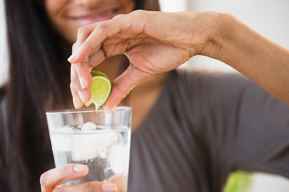 A woman squeeying lime juice in a glass of water with ice cubes
