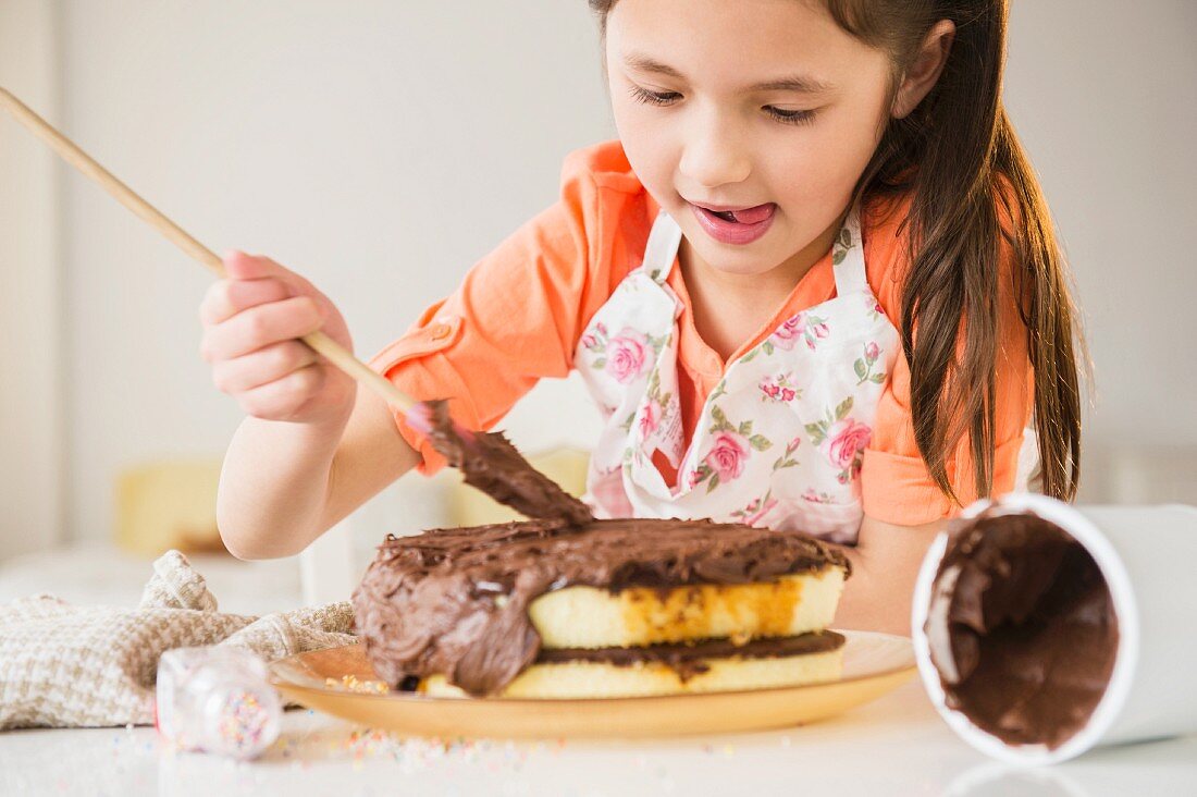 A girl spreading chocolate cream onto a cake