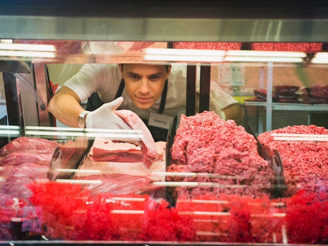 Verkäufer nimmt Fleisch aus Verkaufsvitrine einer Fleischerei