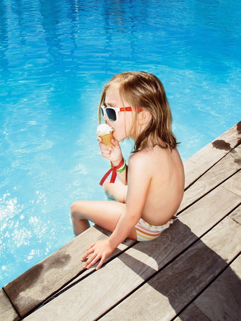 Kleines Mädchen mit Eis an einem Pool sitzend