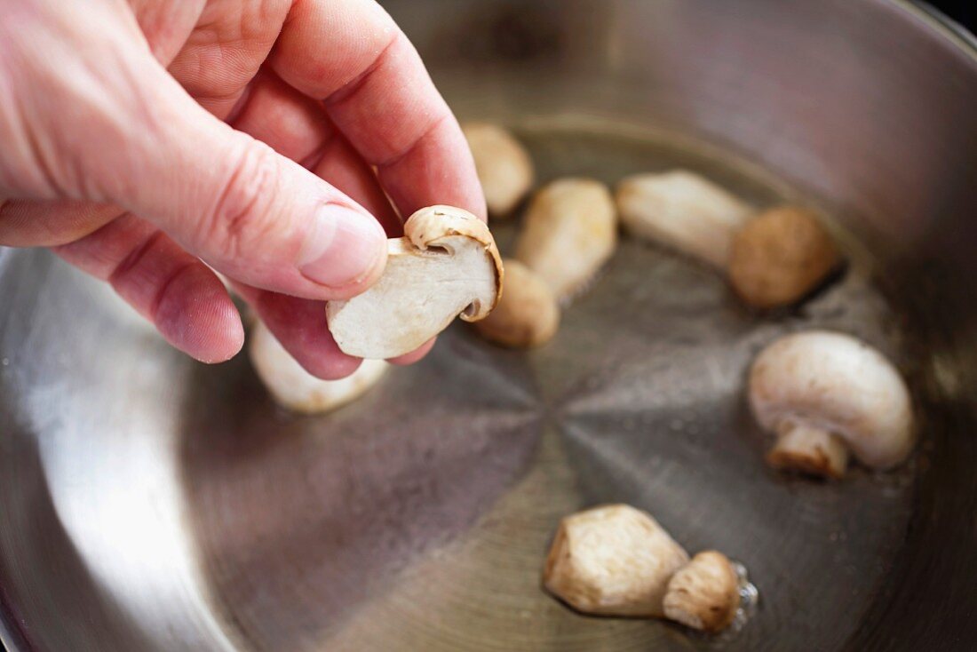 A hand holds a button mushroom above a pot for mushroom cream soup