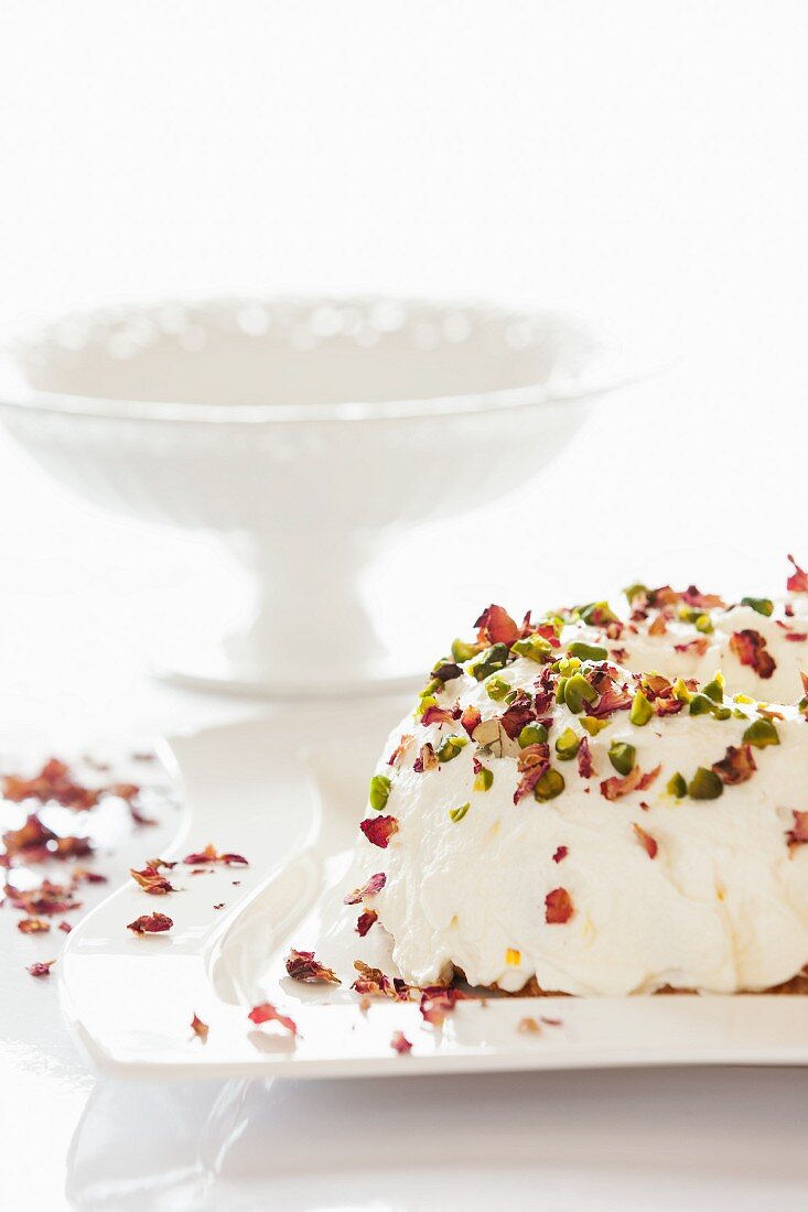 A Bundt cake with white glaze, pistachios and rose petals