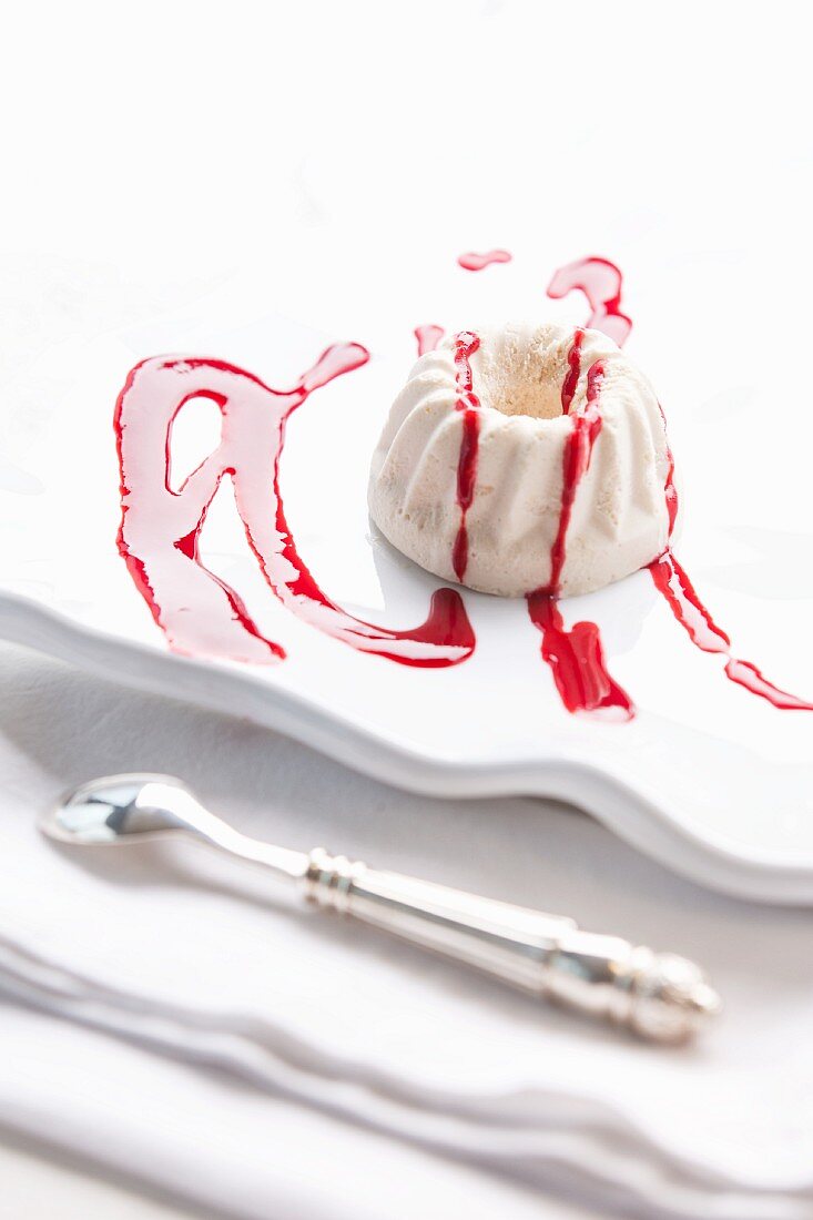 A mini Bundt cake with icing sugar and fruit sauce