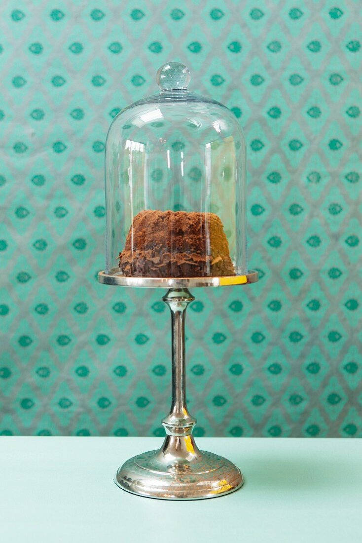A mini Bundt cake under a glass cloche on a cake stand