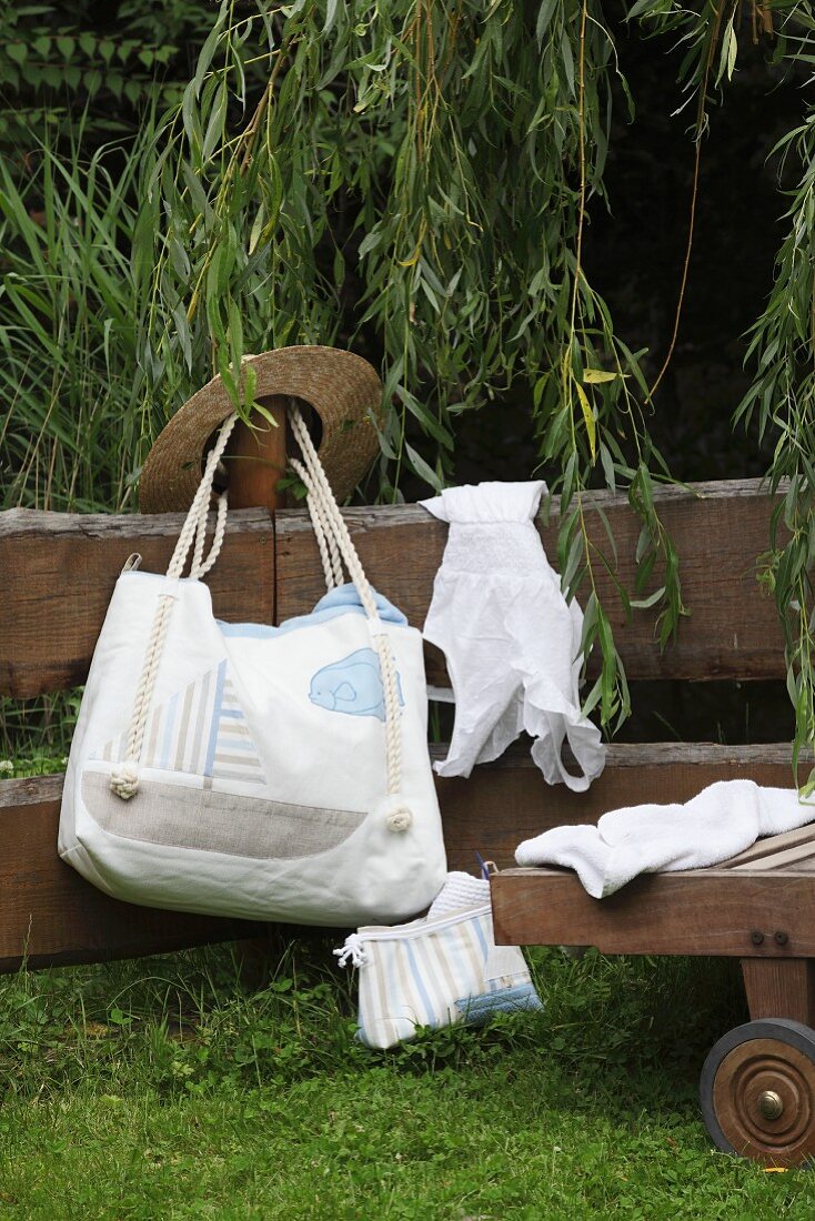 Hand-sewn beach bag with sailing boat motif and cord handles hanging on wooden fence