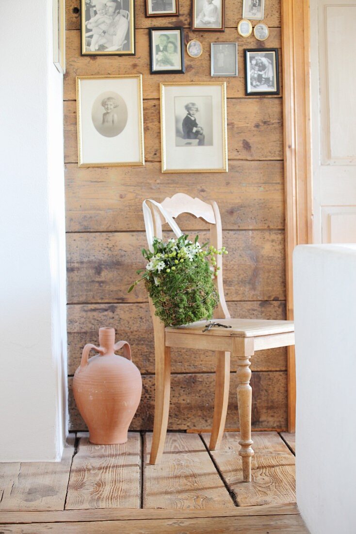 Romantic, bag-shaped arrangement of moss, mistletoe and Star-of-Bethlehem on wooden chair below gallery of photos on wooden wall