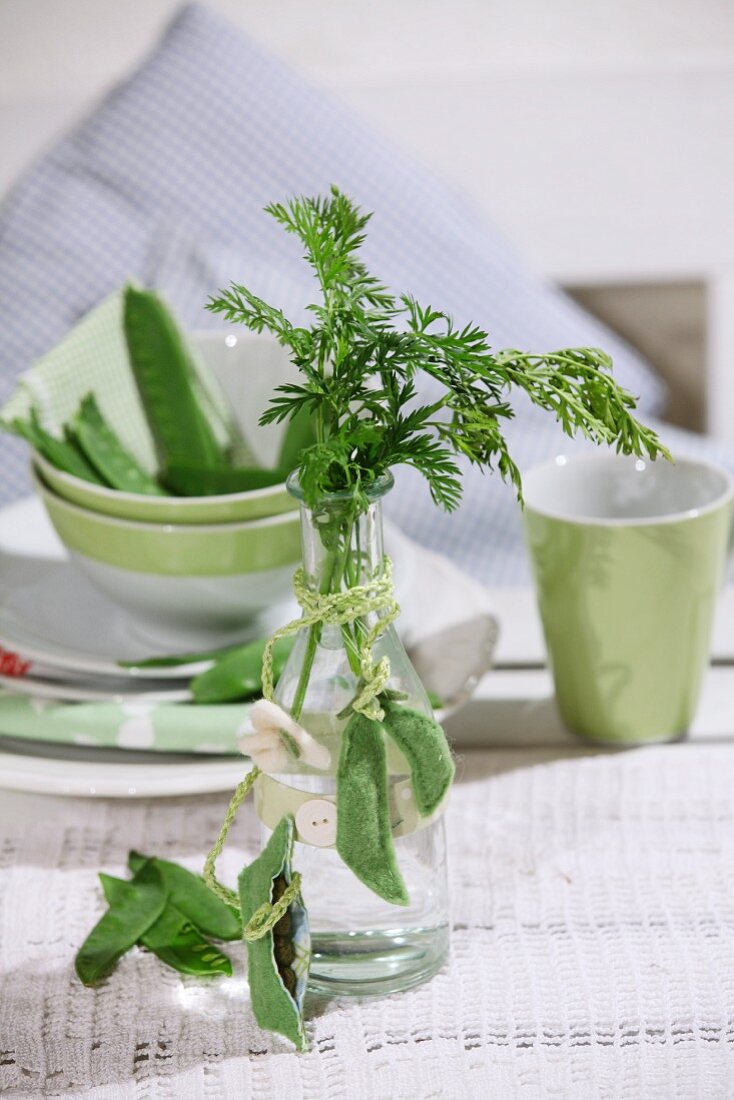 Pale green, felt pea pods draped around small glass vase decorating table