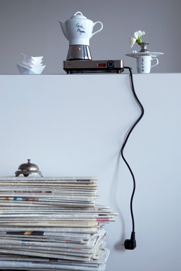 Kochplatte mit Esspressokanne auf Wandbrüstung, davor eine Retro Tischklingel auf einem Zeitungsstapel