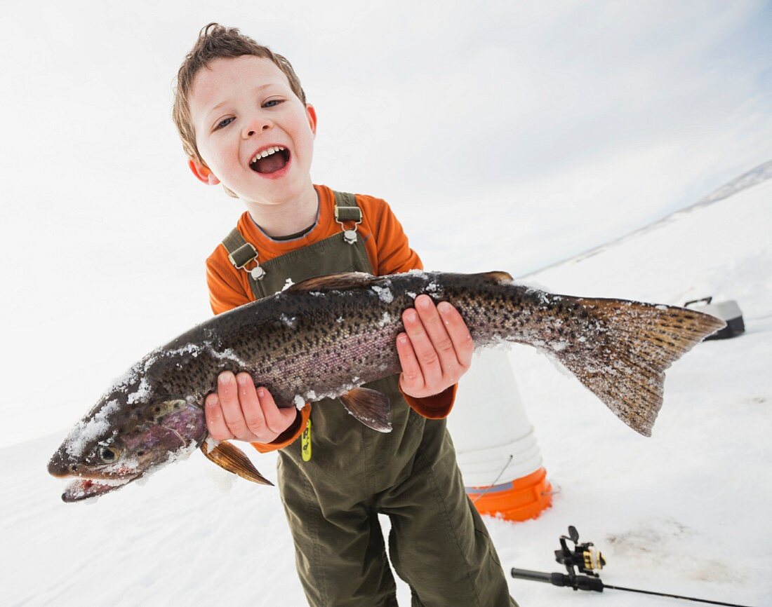 Kleiner Junge beim Eisfischen mit frischgefangenem Fisch