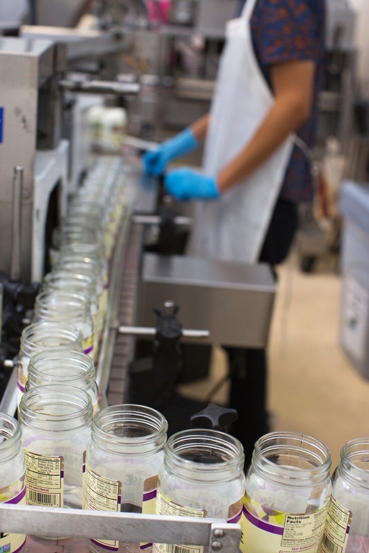 Person operating conveyor belt of empty preserving jars