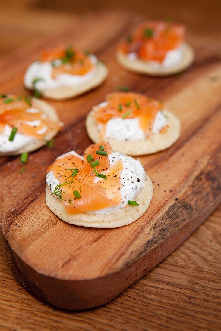 Blinis mit Räucherlachs, Sauerrahm und Schnittlauch auf Holzbrett