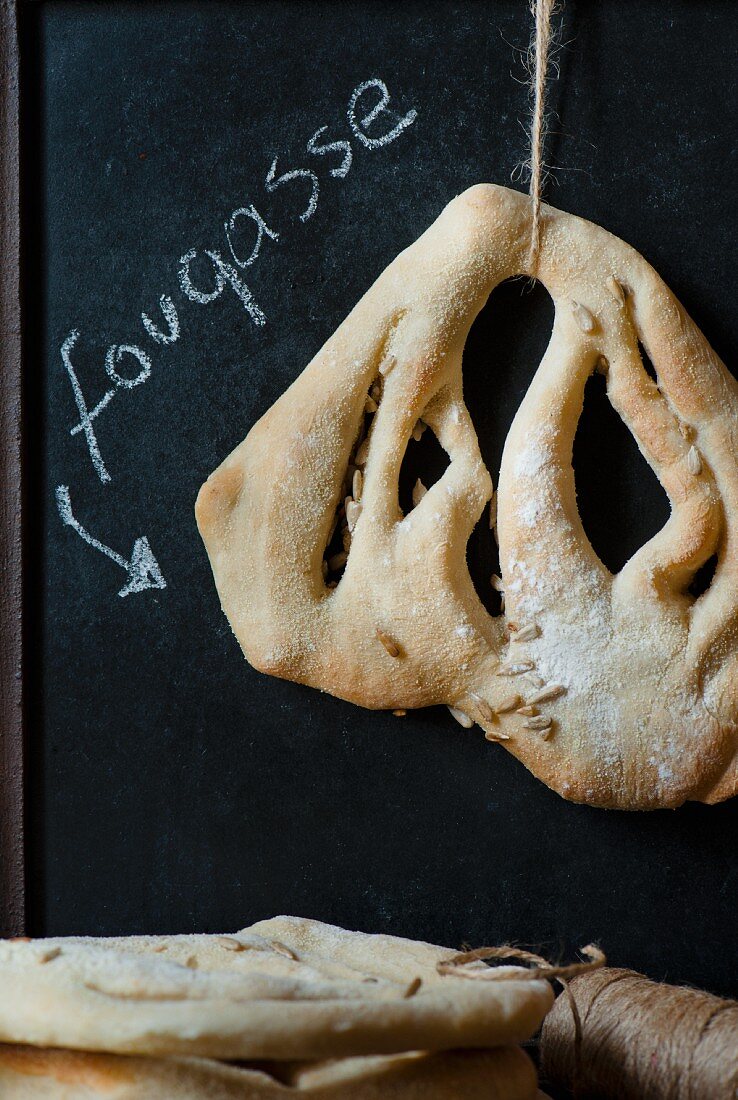 A single Fougasse bread hanging with a sign written in chalk behind.