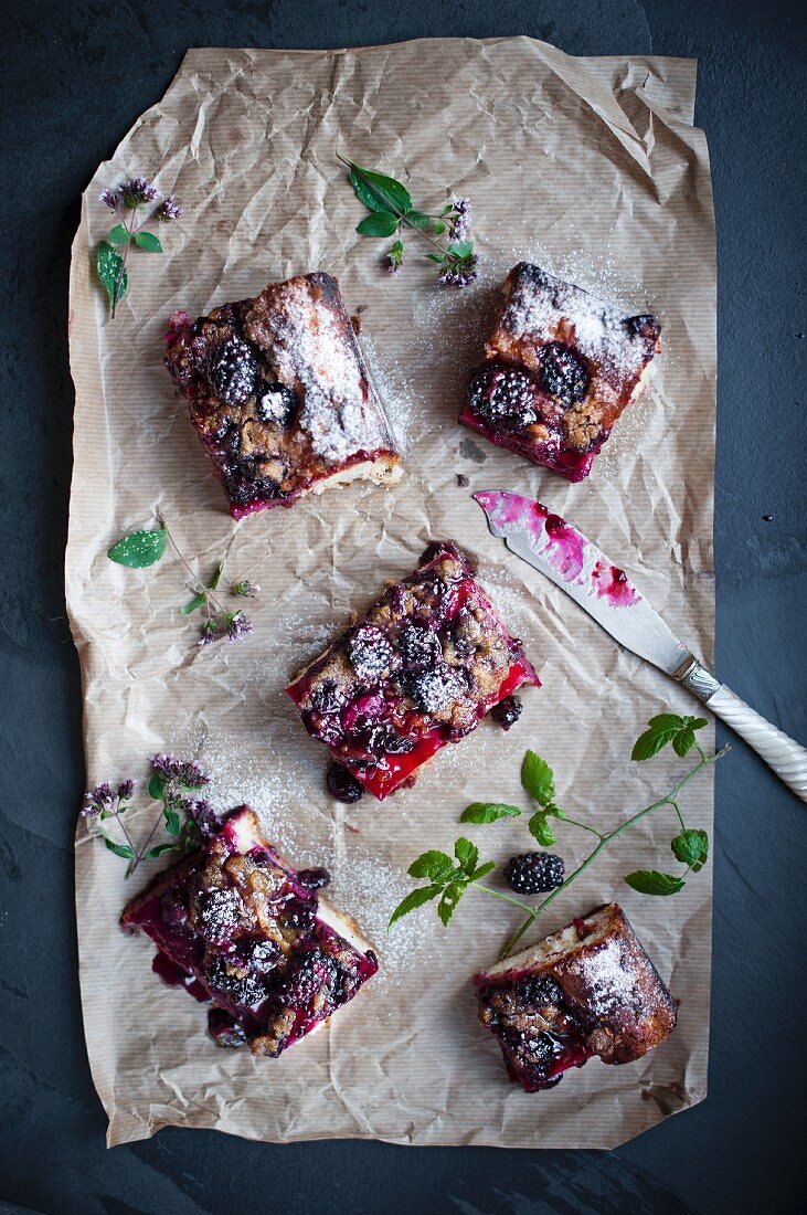 Slices of blackberry cake on brown parchment with a knife and leaves.