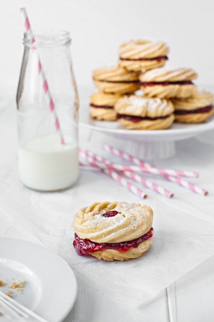 Jam biscuits with a small bottle of milk and pink straws.