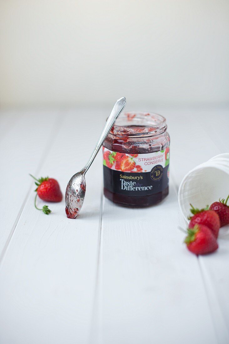 Ein Glas industrielle Erdbeermarmelade mit Löffel und frischen Erdbeeren