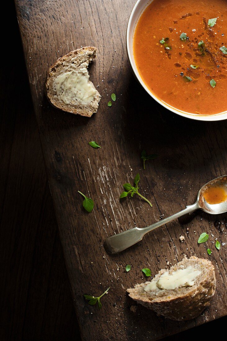 A bowl of fresh tomato soup with slices of buttered bread, fresh basil an spoon.