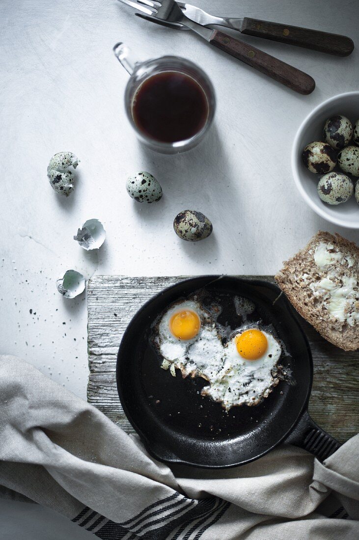Quail eggs fried with a buttered bread and a mug of coffee.