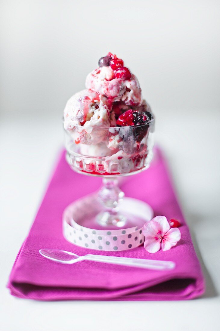 Scoops of summer berry ice cream in a single glass with spoon