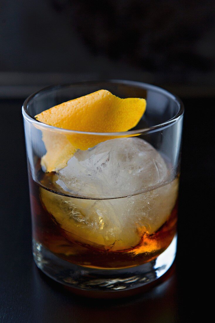 Whiskey im Glas mit grossem Eiswürfel und Orangenschale