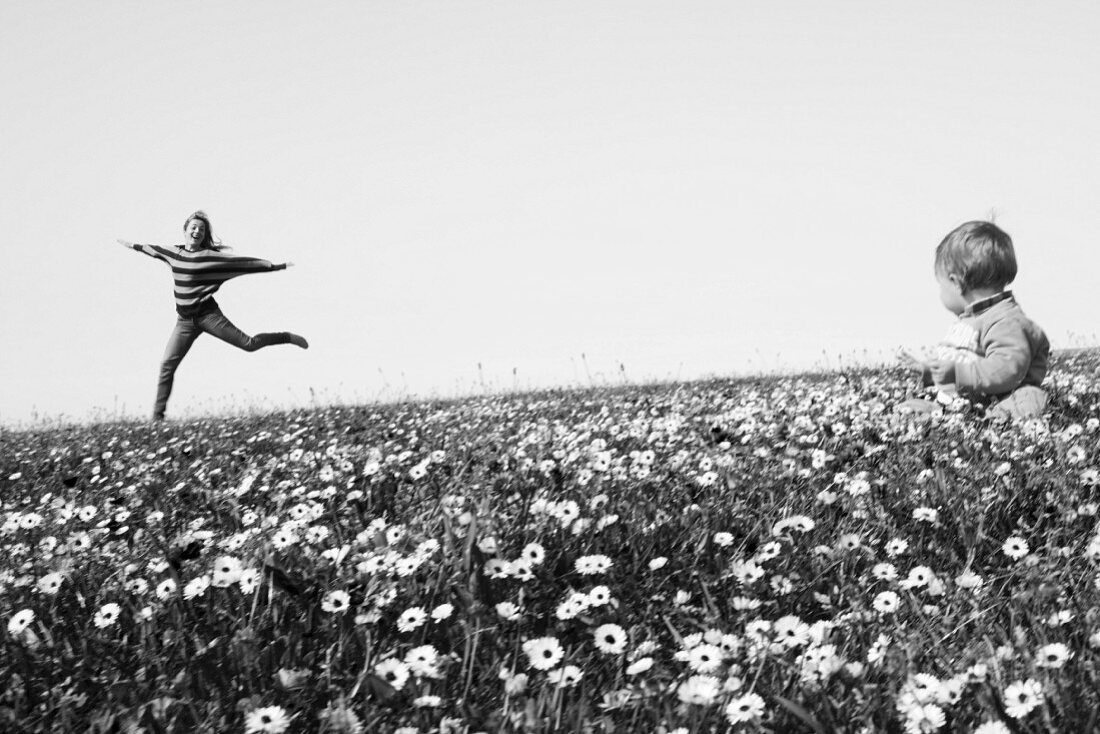 Woman skipping cheerfully though field of wildflowers and baby sitting in foreground