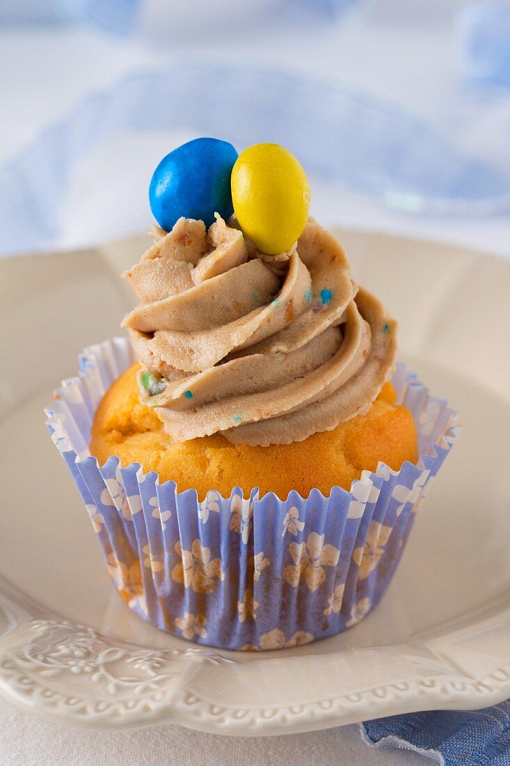 A cupcake decorated with buttercream and coloured chocolate beans