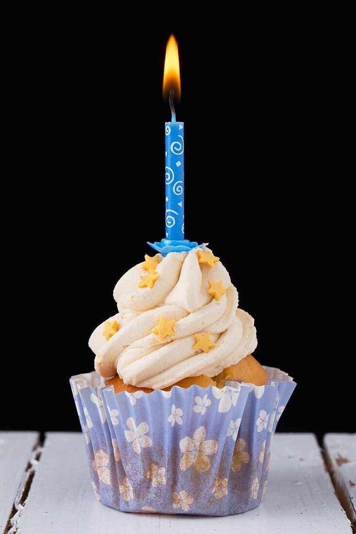 A cupcake decorated with gold stars and a birthday candle