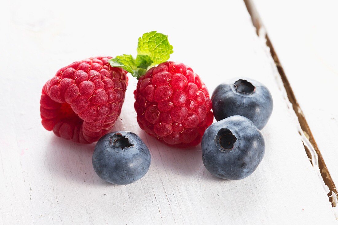 Raspberries and blueberries on a white wooden table